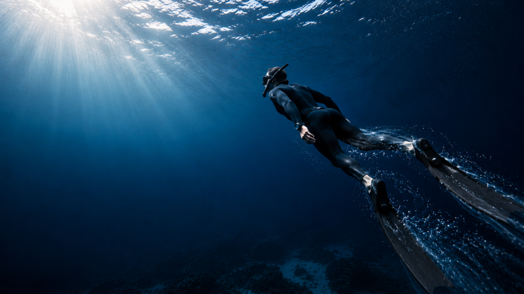 غواص غوص حر يؤدي Hypoxic Dynamic Training بحركة ديناميكية تحت الماء، متجهًا نحو سطح البحر في مشهد يرمز إلى تحسين تحمل نقص الأكسجين وزيادة كفاءة استخدام الأكسجين أثناء الغوص الحر.